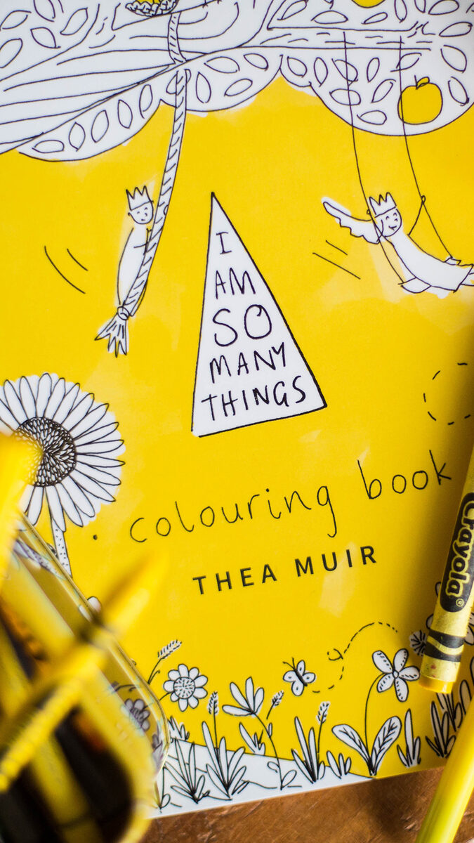 Yellow 'I Am So Many Things' colouring book cover by Thea Muir, with crayons resting on top